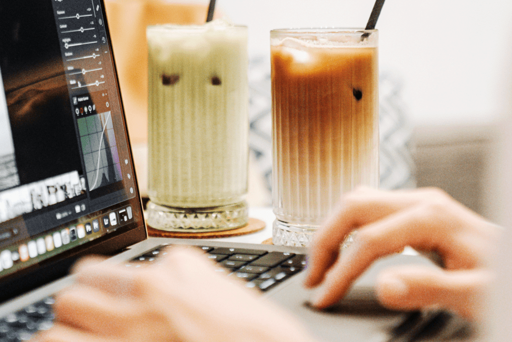 Personne travaillant sur un ordinateur portable dans un café, avec des boissons en gros plan, symbolisant le travail nomade en freelance.